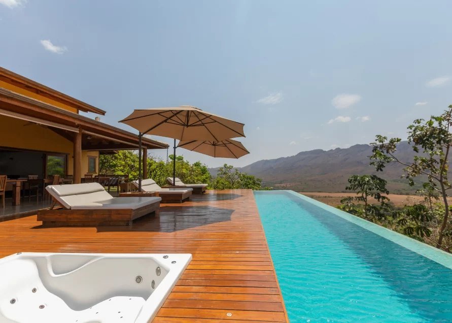 Deck de madeira com espreguiçadeiras, ombrelones e piscina de borda infinita voltada para a Serra